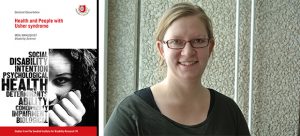 Moa med håret i hästsvans, glasögon och grå tröja står mot en ljusgrå vägg