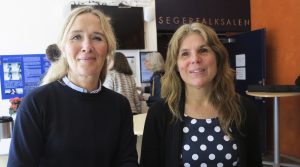 Ann-Charlotte till vänster har mörk tröja och ljust hår i svans, Sara till höger har halvlångt cendréfärgat hår och blommig klänning.