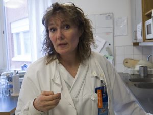 Cathrine i ljust lockigt hår och vit rock står och pratar.