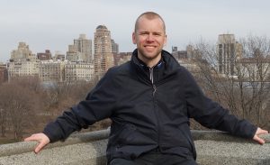 Richard Sahlin i svart jacka står mot en balustrad. Bakom honom ser man storstaden.