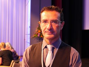 Albergo Gallace med kort mörkt hår, glasögon och mörk väst över en ljust grå skjorta