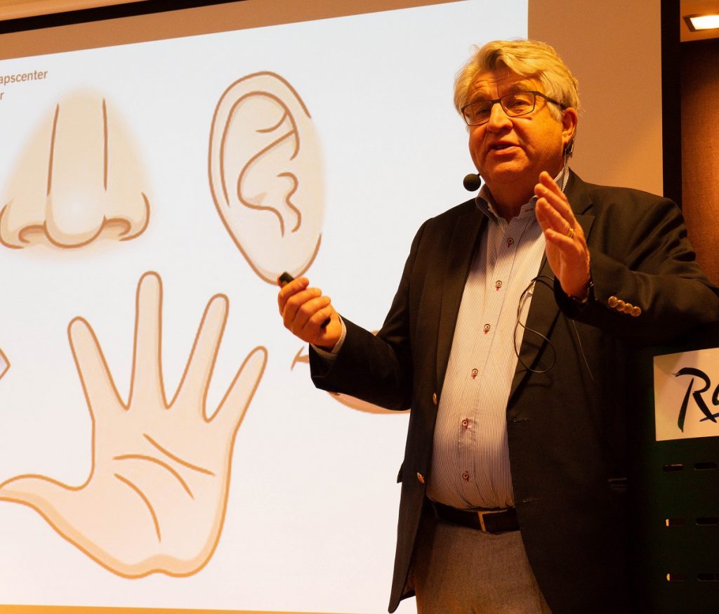 Claes Möller står framför en powerpointbild av en nästa, ett öra och en hand