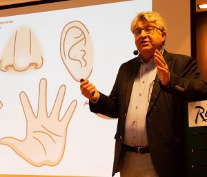 Claes Möller står framför en powerpointbild av en nästa, ett öra och en hand