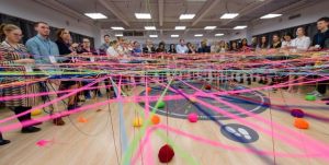 många människor står i en halvcirkel, fokus är på garnerna i olika självlysande färger som bildar ett nät