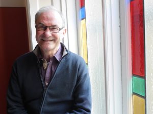 Per i skjorta oc tröja framför ett blyinfattat fönster i blått, gult, grönt och rött.