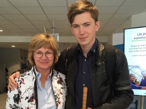 Irene kort ljust hår med glasögon till vänster, Ljus, blommig kavaj, Kristofer är längre och har armen om Irene. Han har mörkblå skjorta under jackan och rödvit käpp i handen.