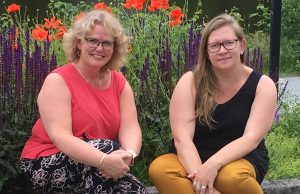 Agneta i ljust lockigt hår, glasögon och rött linje till vänster, Moa i runt långt hår, glasögon ochs vart linne. Båda sitter och i bakgrunden syns röda vallmo