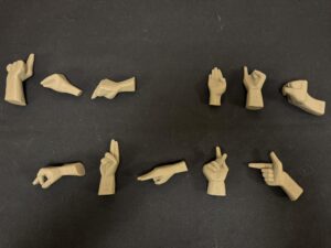 Plasthänder där varje hand gör en av bokstäverna i handalfabetet ligger på en svart yta. Händerna stavar ut "Lär dig punkt". Foto.