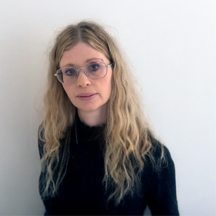 Porträtt på Camilla Falkegård. Hon har lockigt långt ljust hår och glasögon