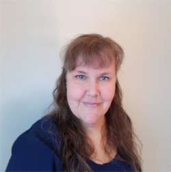 Porträtt på Anneli Johansson. Hon har långt brunt hår och lugg och bär en blå tröja.